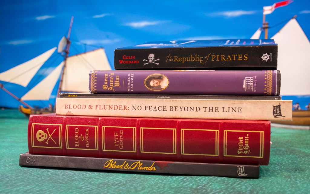Pile of Pirate related Books with Blood & Plunder ship models int he background