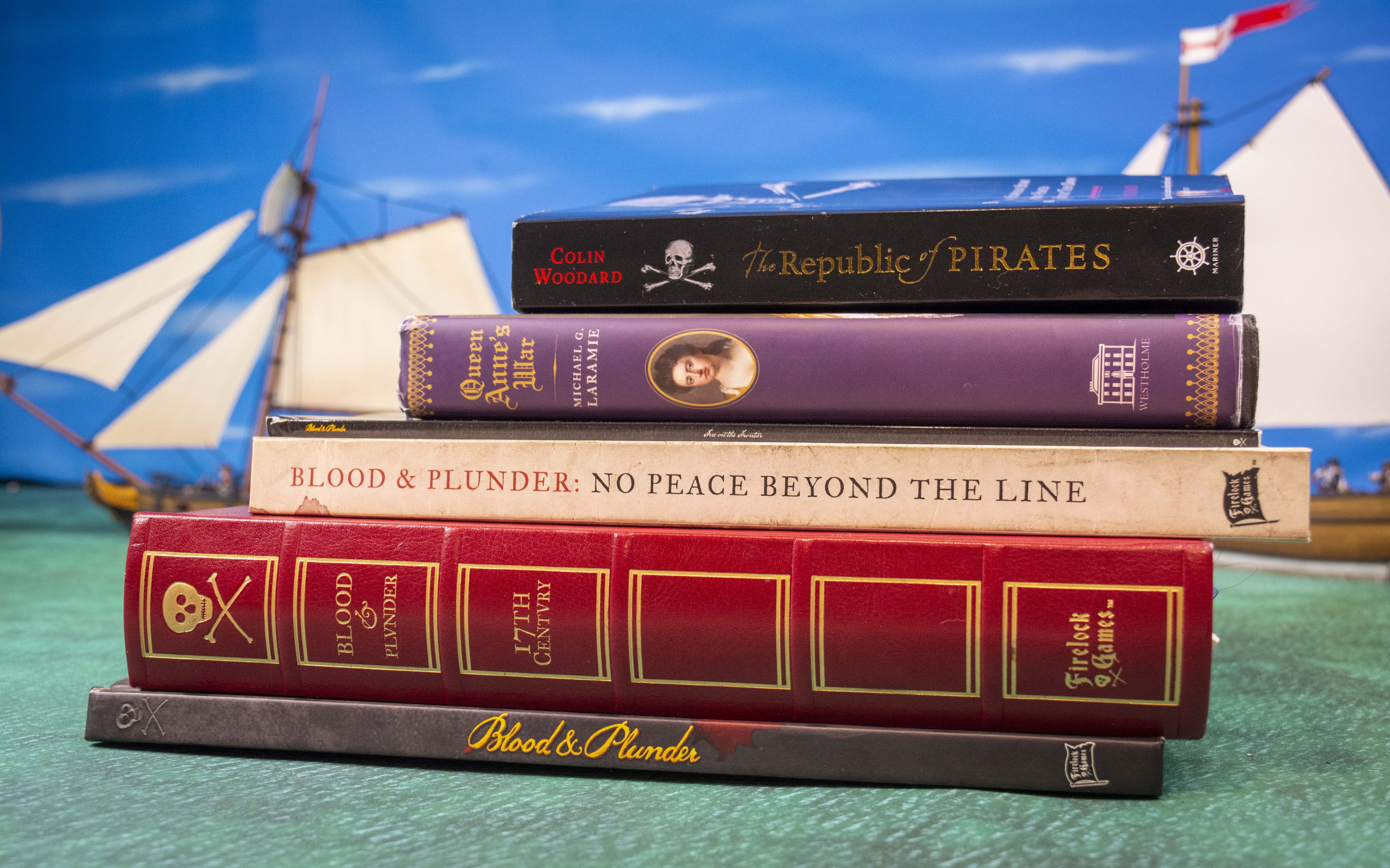 Pile of Pirate related Books with Blood & Plunder ship models int he background