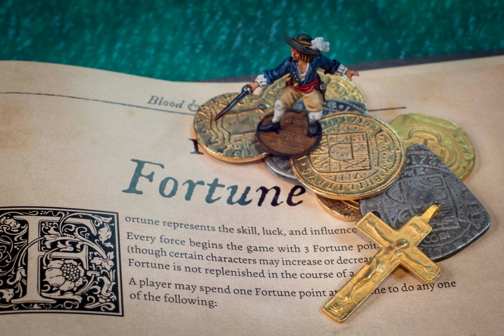Fortune tokens on top of the Blood & Plunder rulebook with a Laurens DeGraff mini on top