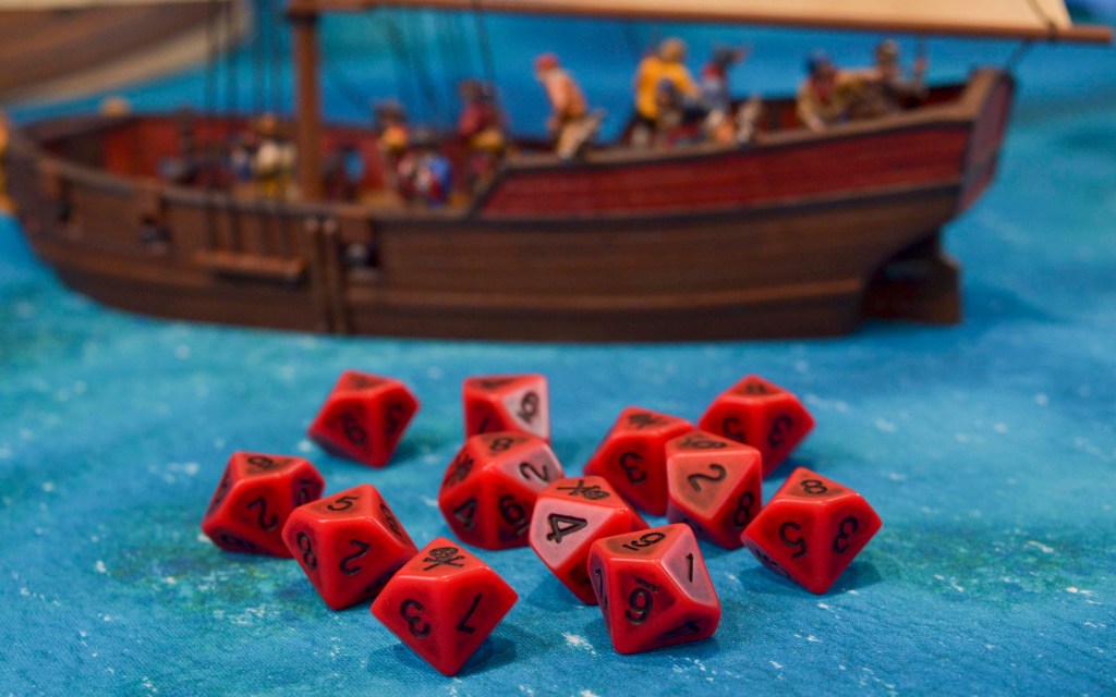 Pile of dice in front of a sloop miniature