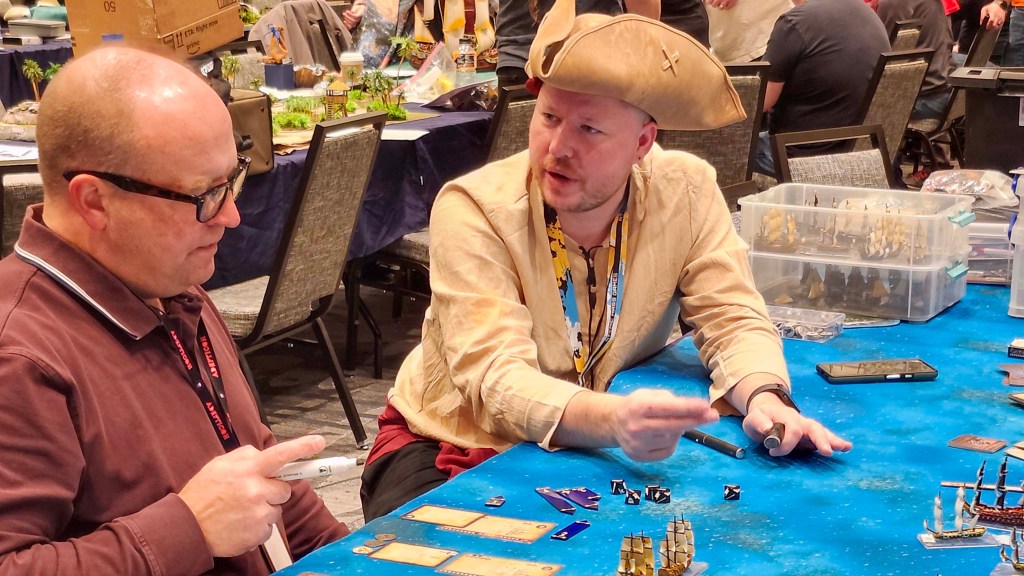 Firelock Games QUartermaster Josh Shivak explains the game of Oak & Iron to a new player.  Sailing ships on a wargaming tabletop gaming mat